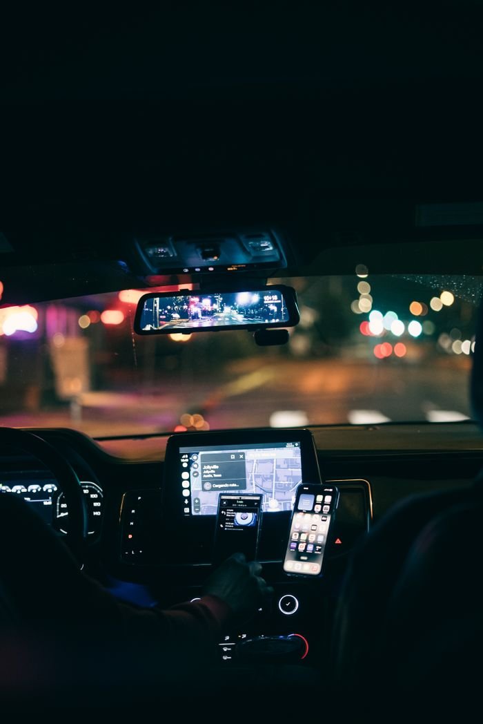 A car interior at night showing GPS navigation on a smartphone with city lights in the background.